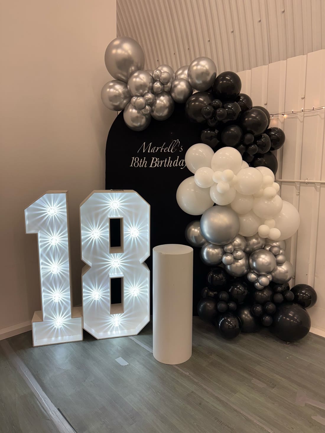 18th birthday backdrop with light-up number 18, black name board & balloon garland arch