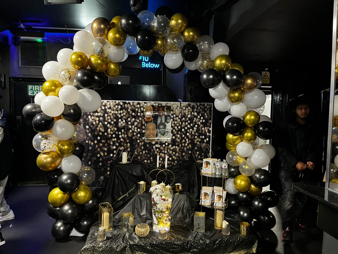 Black and gold balloon arch framing a celebration-of-life memory table